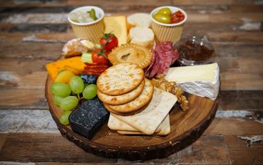 Board of cheese, crackers, grapes, olives, pickles and chutney.