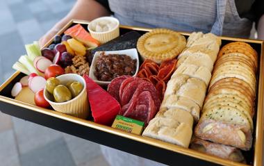 Board of cheese, crackers, bread roll and accompanying foods.