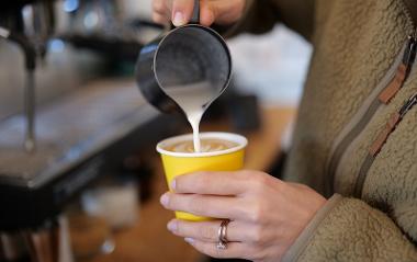 Close up of trader pouring milk into coffee cup